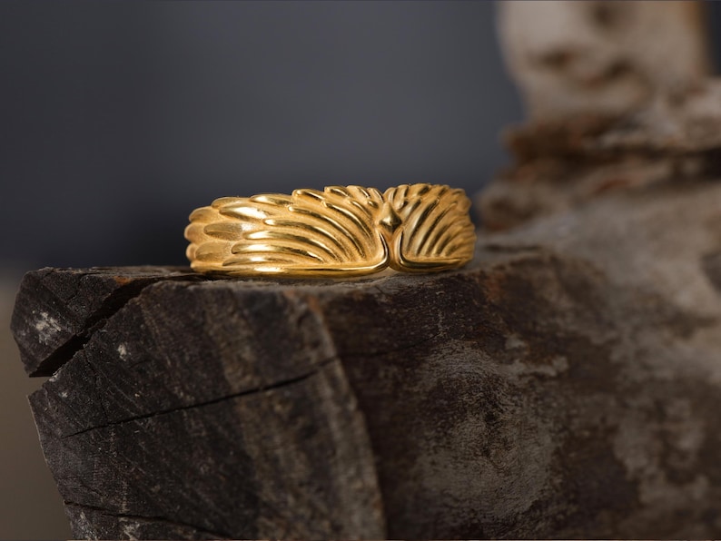 May include: A gold ring with a textured design resembling a pair of wings.