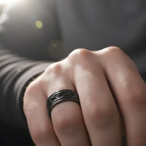 Puede incluir: Primer plano de un anillo negro con un dise&ntilde;o intrincado y ondulado. El anillo est&aacute; en una mano, mostrando el dise&ntilde;o detallado. El anillo, probablemente de metal, tiene un acabado mate.