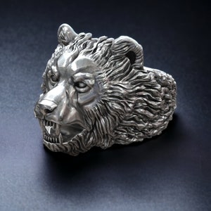 Roaring bear head ring, wild animal inspired statement jewelry, symbolic warrior band, and handcrafted bold accessory designed for those who are drawn to strength, dominance, and fearless energy. This striking ring features a detailed roaring bear head motif with open jaws, sharp teeth, and intense engraved textures, creating a powerful and aggressive appearance inspired by nature, Viking symbolism, and primal force.