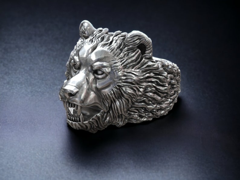 Roaring bear head ring, wild animal inspired statement jewelry, symbolic warrior band, and handcrafted bold accessory designed for those who are drawn to strength, dominance, and fearless energy. This striking ring features a detailed roaring bear head motif with open jaws, sharp teeth, and intense engraved textures, creating a powerful and aggressive appearance inspired by nature, Viking symbolism, and primal force.