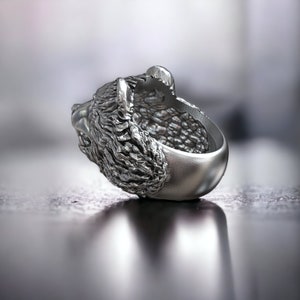 Roaring bear head ring, wild animal inspired statement jewelry, symbolic warrior band, and handcrafted bold accessory designed for those who are drawn to strength, dominance, and fearless energy. This striking ring features a detailed roaring bear head motif with open jaws, sharp teeth, and intense engraved textures, creating a powerful and aggressive appearance inspired by nature, Viking symbolism, and primal force.