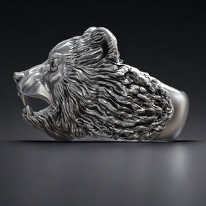 Roaring bear head ring, wild animal inspired statement jewelry, symbolic warrior band, and handcrafted bold accessory designed for those who are drawn to strength, dominance, and fearless energy. This striking ring features a detailed roaring bear head motif with open jaws, sharp teeth, and intense engraved textures, creating a powerful and aggressive appearance inspired by nature, Viking symbolism, and primal force.