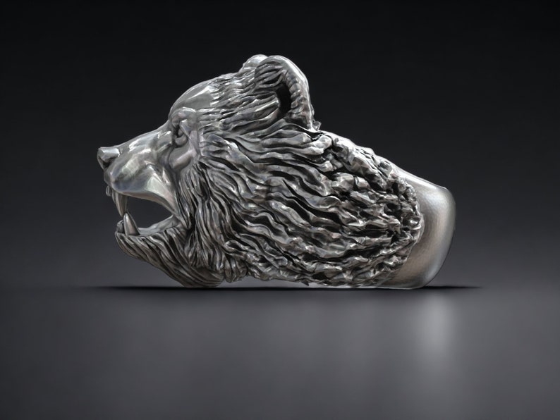 Roaring bear head ring, wild animal inspired statement jewelry, symbolic warrior band, and handcrafted bold accessory designed for those who are drawn to strength, dominance, and fearless energy. This striking ring features a detailed roaring bear head motif with open jaws, sharp teeth, and intense engraved textures, creating a powerful and aggressive appearance inspired by nature, Viking symbolism, and primal force.