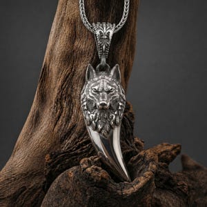 Op de afbeelding: Een zilverkleurige hangerketting met een gedetailleerd wolfskopontwerp. De hanger is bevestigd aan een zilveren ketting. De wolfskop heeft ingewikkelde details, met een felle uitdrukking. De hanger is gevormd als een wolfstand.