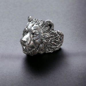 Roaring bear head ring, wild animal inspired statement jewelry, symbolic warrior band, and handcrafted bold accessory designed for those who are drawn to strength, dominance, and fearless energy. This striking ring features a detailed roaring bear head motif with open jaws, sharp teeth, and intense engraved textures, creating a powerful and aggressive appearance inspired by nature, Viking symbolism, and primal force.