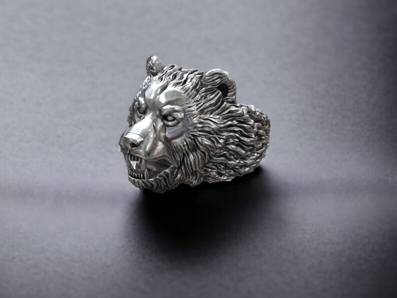 Roaring bear head ring, wild animal inspired statement jewelry, symbolic warrior band, and handcrafted bold accessory designed for those who are drawn to strength, dominance, and fearless energy. This striking ring features a detailed roaring bear head motif with open jaws, sharp teeth, and intense engraved textures, creating a powerful and aggressive appearance inspired by nature, Viking symbolism, and primal force.