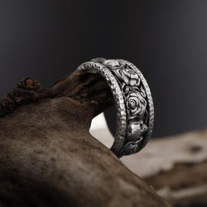 K&ouml;nnte beinhalten: Ein silberner Ring mit einem detaillierten Design aus Rosen und Bl&auml;ttern. Der Ring ist texturiert und hat eine geh&auml;mmerte Oberfl&auml;che.