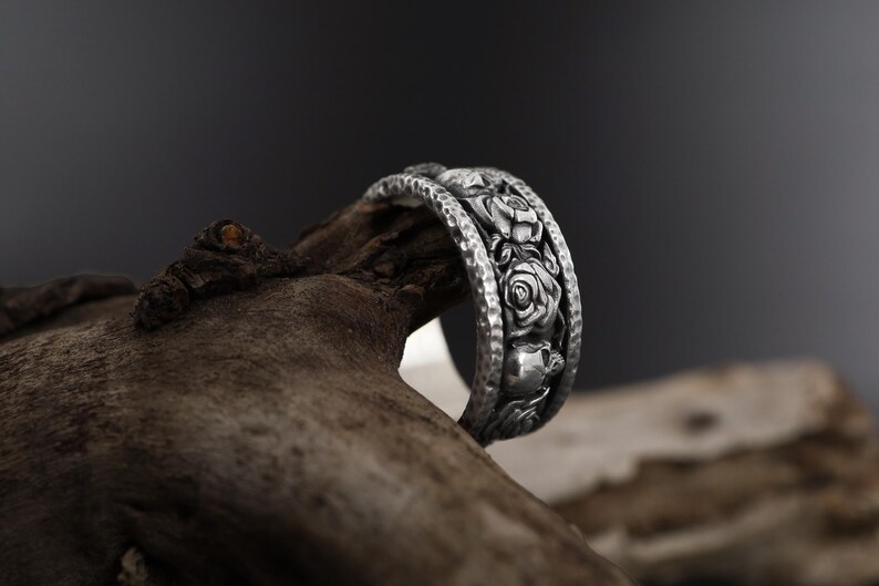 K&ouml;nnte beinhalten: Ein silberner Ring mit einem detaillierten Design aus Rosen und Bl&auml;ttern. Der Ring ist texturiert und hat eine geh&auml;mmerte Oberfl&auml;che.
