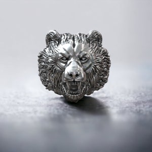Roaring bear head ring, wild animal inspired statement jewelry, symbolic warrior band, and handcrafted bold accessory designed for those who are drawn to strength, dominance, and fearless energy. This striking ring features a detailed roaring bear head motif with open jaws, sharp teeth, and intense engraved textures, creating a powerful and aggressive appearance inspired by nature, Viking symbolism, and primal force.