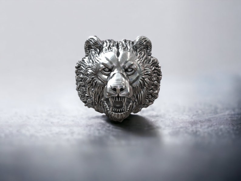 Roaring bear head ring, wild animal inspired statement jewelry, symbolic warrior band, and handcrafted bold accessory designed for those who are drawn to strength, dominance, and fearless energy. This striking ring features a detailed roaring bear head motif with open jaws, sharp teeth, and intense engraved textures, creating a powerful and aggressive appearance inspired by nature, Viking symbolism, and primal force.