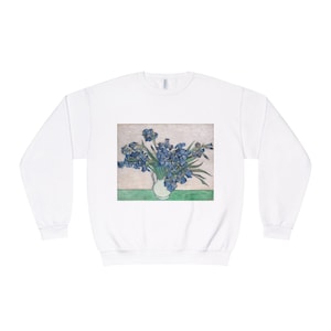 May include: White sweatshirt featuring a print of a vase of blue irises, a famous painting by Vincent van Gogh. The artwork is set against a neutral background with a green base. The sweatshirt has a crew neck and long sleeves.