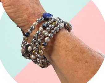 Puede incluir: Un conjunto de pulseras de cuentas en varios tonos de gris, plata y transparente. Las pulseras presentan una mezcla de cuentas facetadas, perlas y detalles metálicos. Una sola cuenta de piedra azul es visible en la parte superior.