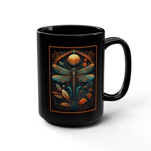 May include: Black ceramic mug with a dragonfly illustration in gold, teal, and orange colors. The dragonfly is surrounded by floral elements and a crescent moon.