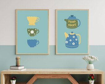 May include: Two framed prints with a blue background. The print on the left features three teacups stacked on top of each other. The top cup is yellow, the middle cup is green with a white flower, and the bottom cup is blue. The print on the right features two teapots. The top teapot is green with a yellow lid and the bottom teapot is blue with white flowers.