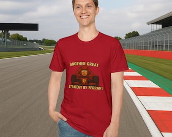 May include: A red t-shirt featuring a cartoon illustration of a person in a racing car. The text on the shirt reads "Another Great Strategy by Ferrari".