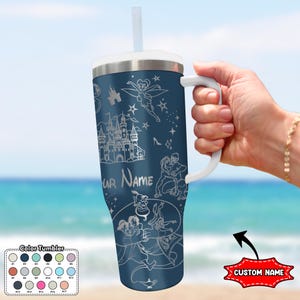 May include: A navy blue tumbler with a white handle and straw, featuring etched illustrations of a castle, Tinkerbell, and other characters. The text "YOUR NAME" is visible. A color chart and "CUSTOM NAME" text are also present.
