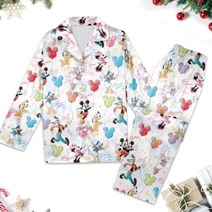 May include: White pajama set featuring a colorful print of Disney characters like Mickey Mouse, Minnie Mouse, Donald Duck, and Goofy holding balloon bouquets. The long-sleeved top and pants are decorated with pastel-colored balloons and character signatures.