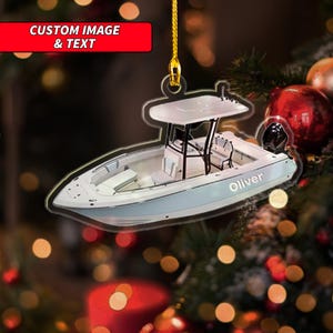 May include: A boat-shaped Christmas ornament with a light blue hull and white detailing. The ornament features a cabin, seats, and the name "Oliver". The top of the ornament has the text "CUSTOM IMAGE & TEXT" in a red rectangle.