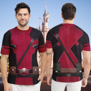 May include: A red and black t-shirt featuring a Deadpool costume design. The front of the shirt has a belt with a Deadpool logo, pouches, and straps. The back of the shirt also features the costume design with straps and pouches.