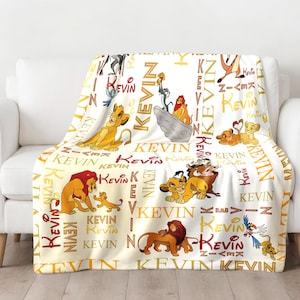 May include: A white fleece throw blanket with a repeating pattern of the Lion King characters and the name "Kevin" in gold lettering.