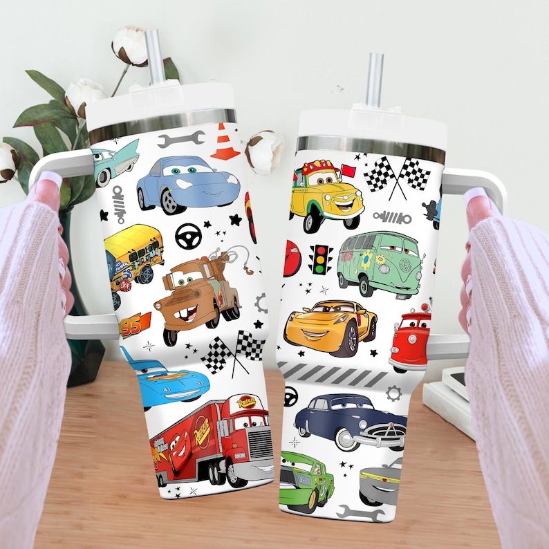 May include: Two white insulated tumblers with a variety of cartoon car illustrations. The cars are in different colors, including blue, yellow, and red. Each tumbler has a white lid and a silver straw.