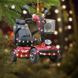 May include: A red mobility scooter Christmas ornament with a black seat and basket. The ornament is decorated with colourful lights and has the text "CUSTOM NAME" on the side. The scooter has a headlight and a gold-coloured hanger.