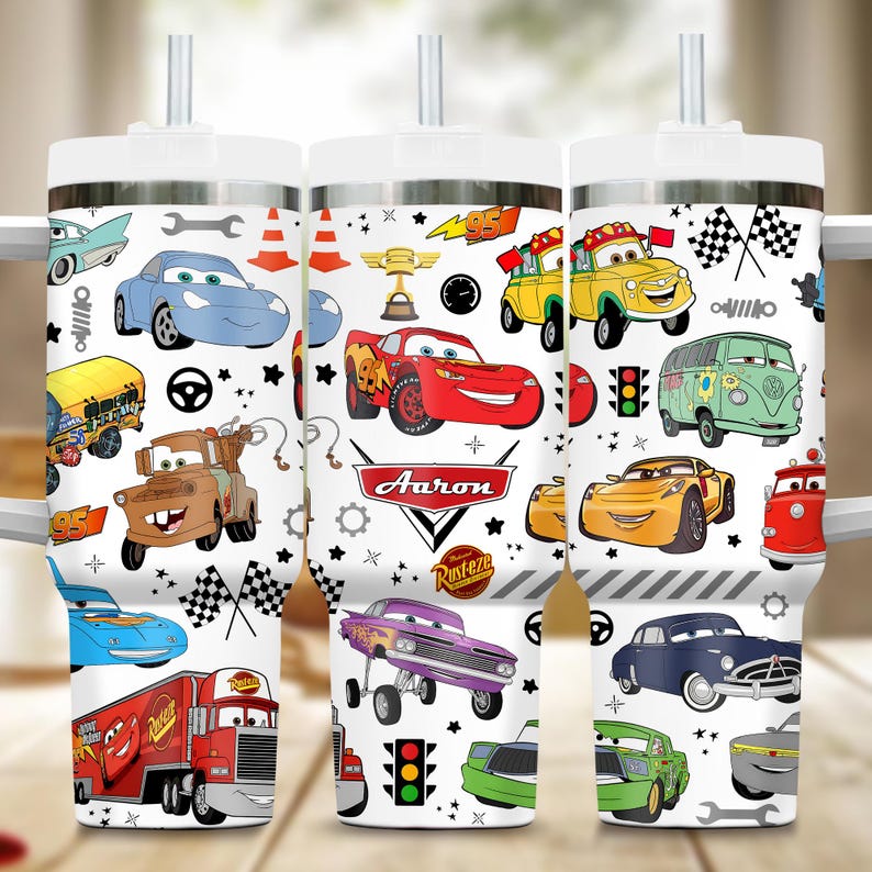 May include: White tumbler featuring a colorful cartoon car design. The design includes various car characters, racing flags, and the name "Aaron". The tumbler has a white lid and a straw.