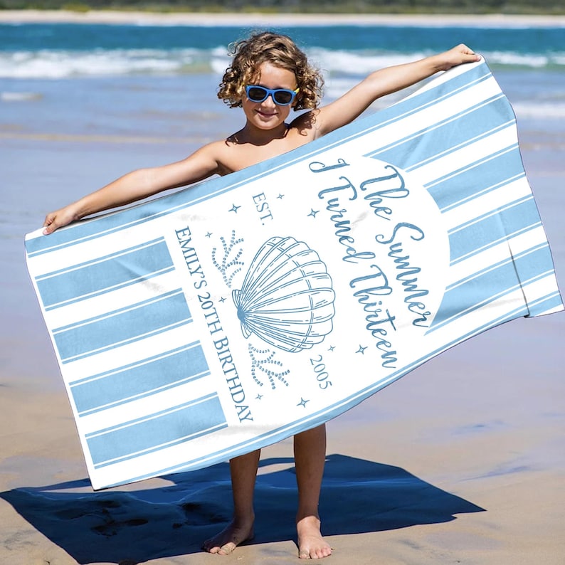 May include: A light blue and white striped beach towel with the text "The Summer I Turned Thirteen" and "Emily's 20th Birthday" in a decorative font. The towel features a seashell graphic and is held by a person on a beach.