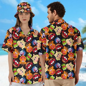 May include: Two people wearing black and white short-sleeved button-down shirts with a repeating pattern of colourful Muppet characters. The shirt has a relaxed fit and a collar.