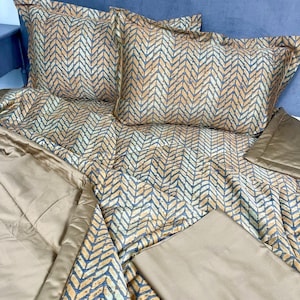 May include: A beige duvet cover with a chevron pattern in shades of orange, blue, and white. The duvet cover is folded and displayed on a bed with matching pillowcases.