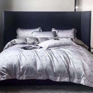 May include: A plush, light grey bed with a dark blue headboard. The bed is made with a white and grey patterned duvet cover and matching pillowcases. The bed is styled with a white and grey patterned throw pillow.