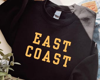 May include: Black sweatshirt with the words "East Coast" in yellow block letters.