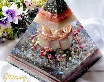 May include: A decorative pyramid made of resin, featuring layers of color and embedded with flowers and glitter. The pyramid has a square base and tapers to a point. The base is approximately 4 inches wide.