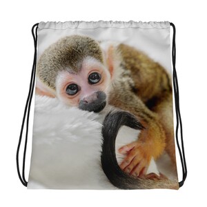 May include: A small brown and white monkey with big eyes is lying on a white fluffy surface. The monkey's tail is curled around its body.