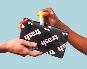 May include: A black zippered pouch with the word "fresh" repeated in white lettering. A hand is placing a yellow tube of hand sanitizer inside the pouch.