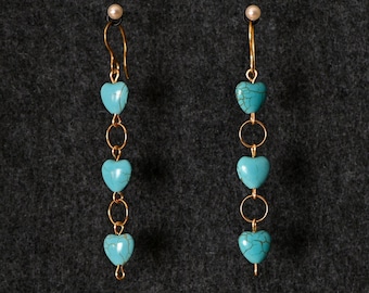 May include: A pair of gold dangle earrings with turquoise heart-shaped beads. The earrings have a simple design with a single bead at the top and three beads hanging below.