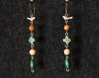 May include: A pair of long, dangling earrings with a white bird charm, brown wooden beads, green and blue cross-shaped beads, and a green wooden bead at the bottom.