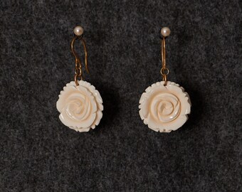 May include: A pair of white carved rose earrings with gold hooks.