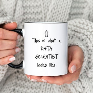 Op de afbeelding: Een witte keramische mok met een zwarte rand en handvat. De mok heeft zwarte tekst die "This is what a DATA SCIENTIST looks like" luidt met een pijl die omhoog wijst.