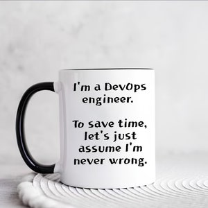 Könnte beinhalten: Eine weiße Keramiktasse mit schwarzem Henkel und schwarzem Rand. Die Tasse hat einen schwarzen Text mit der Aufschrift "Ich bin ein DevOps-Ingenieur. Um Zeit zu sparen, nehmen wir einfach an, dass ich nie falsch liege."
