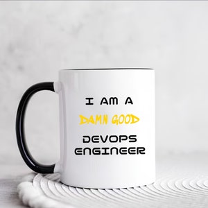 Peut inclure: Une tasse en céramique blanche avec une poignée noire et un bord noir. La tasse porte l'inscription "I am a damn good DevOps Engineer" imprimée en noir et jaune.