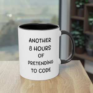 May include: White ceramic coffee mug with a black rim and handle. The mug has black text that reads "Another 8 hours of pretending to code."