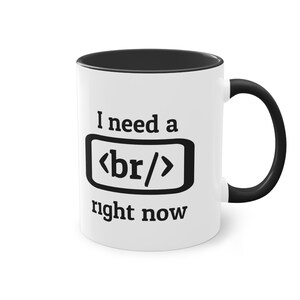 Könnte beinhalten: Weiße Keramik-Kaffeetasse mit schwarzem Rand und Henkel. Die Tasse hat eine schwarze Grafik des HTML-Codes für einen Zeilenumbruch, "<br/>", und den Text "Ich brauche einen jetzt".