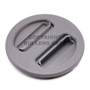 May include: A grey plastic lens cap with two slots for easy removal. The cap is designed to fit a camera lens.