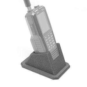 May include: A black handheld radio with a black antenna and a keypad with white numbers and symbols. The radio is sitting in a black plastic charging stand.