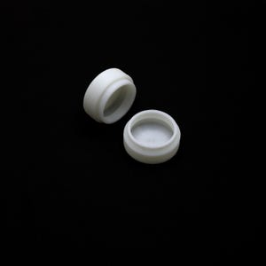 Puede incluir: Dos pequeños recipientes redondos blancos con tapas. Una tapa está abierta, revelando el interior del recipiente. Los recipientes están hechos de un material liso y opaco y se encuentran sobre un fondo negro.
