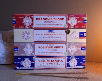 Könnte beinhalten: Vier Schachteln Satya-Räucherstäbchen sind gestapelt, jede mit einem anderen Etikett: Dragon's Blood, Californian White Sage, Positive Vibes und Nag Champa Agarbatti. Die Schachteln sind rot, weiß und blau, mit dem Markennamen und Produktdetails.