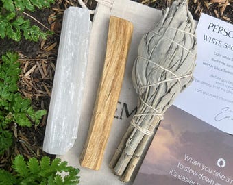 Könnte beinhalten: Ein weißer Selenit-Kristallstab, ein hellbraunes Palo-Santo-Holzstück und ein mit Schnur gebundenes Bündel getrockneter weißer Salbei auf einem beigen Baumwollbeutel neben einer Karte mit dem Text "PERSONALIZED WHITE SAGE".