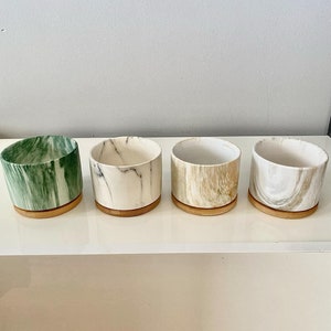 May include: Four small ceramic planters with a marble pattern. Each planter has a wooden base. The planters are green, white, beige, and grey.