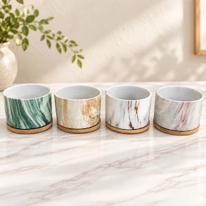 May include: Four cylindrical ceramic planters with marble-effect patterns in green, tan, white with gold veining, and grey with pink streaks. Each planter sits on a circular bamboo saucer and features a smooth, white interior finish.